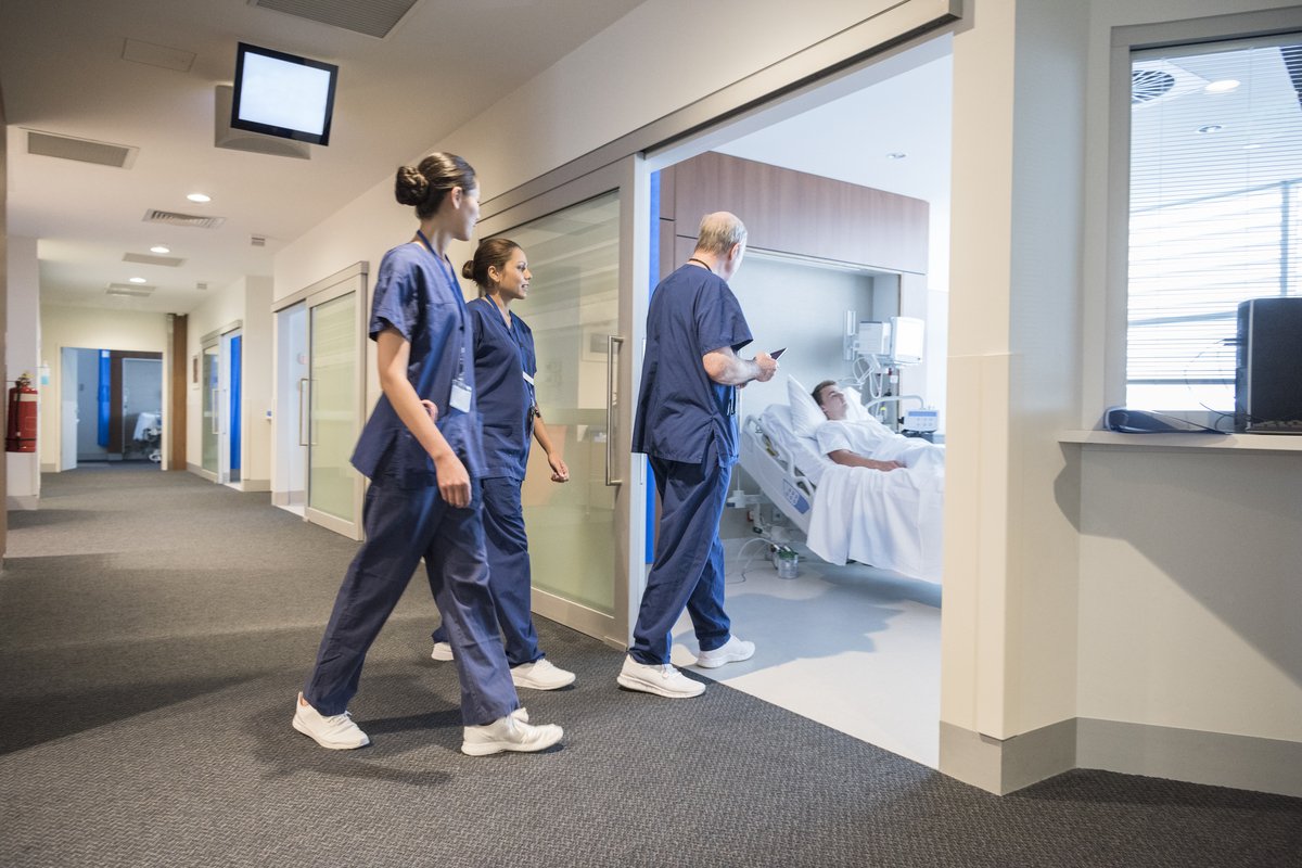 Medical team entering hospital ward where male patient is lying in bed
